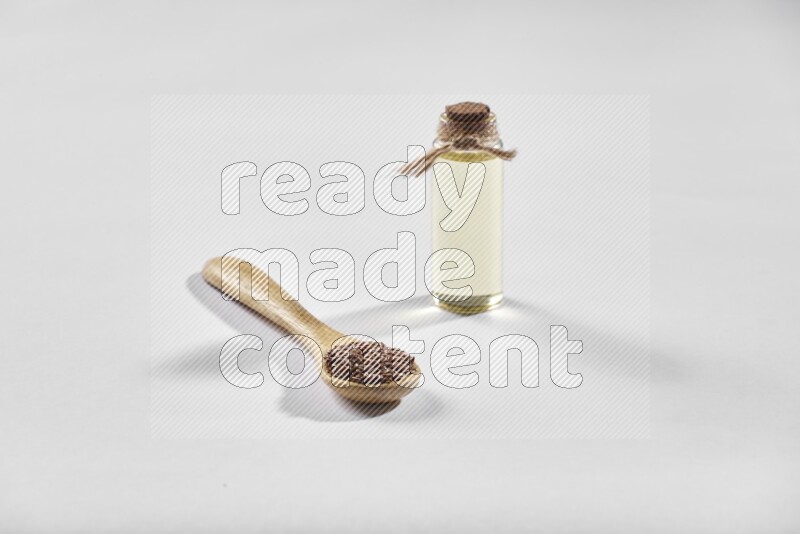A wooden spoon full of flax seeds and a glass bottle full of flaxseeds oil on a white flooring