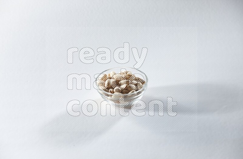 A glass bowl full of pistachios on a white background in different angles
