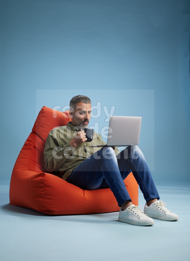 A man sitting on an orange beanbag and working on laptop