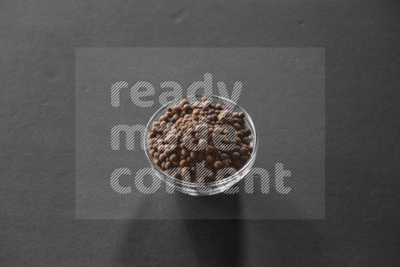 A glass bowl full of allspice on black flooring