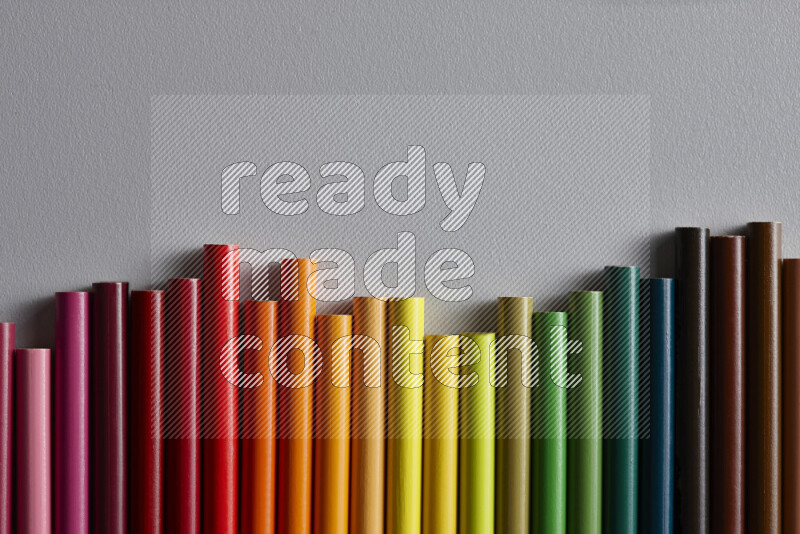 A collection of colored pencils arranged showcasing a gradient of different hues on grey background
