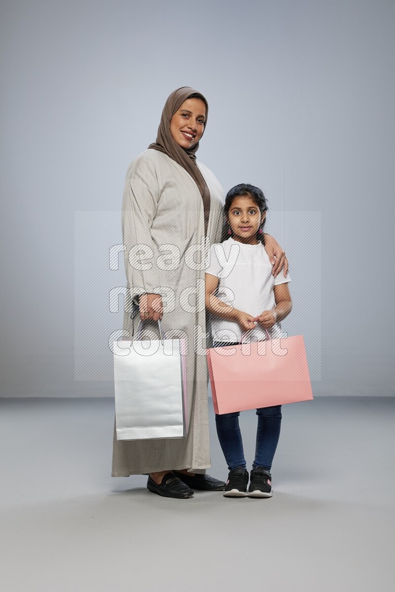 Mom and daughter holding shopping bags on gray background