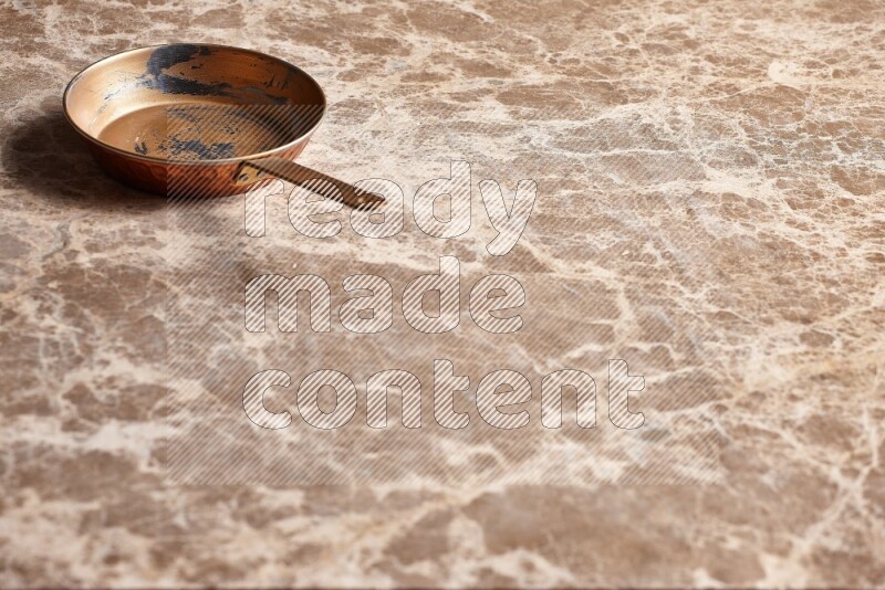 A small copper pan on beige marble background
