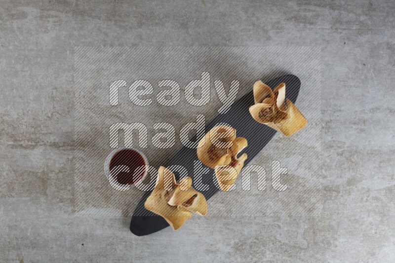 wonton cups with soy sauce ramkin on oval slate on grey textured counter top