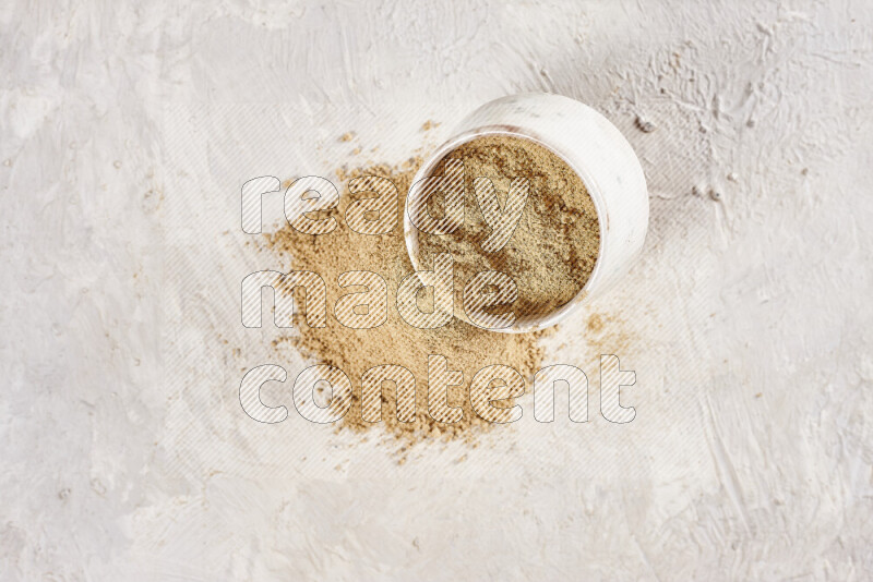 A beige pottery bowl full of ground ginger powder with fallen powder from it on white background