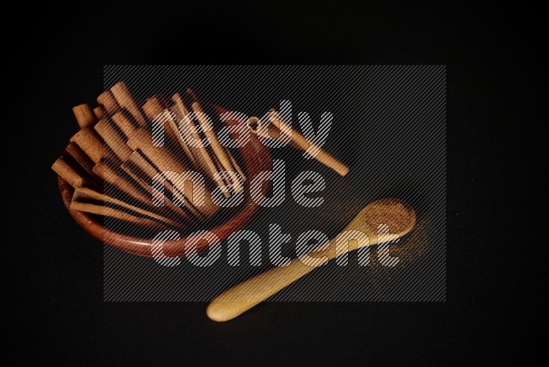 أعواد القرفة في وعاء خشبي وبودرة القرفة في ملعقة خشبية على خلفية سوداء