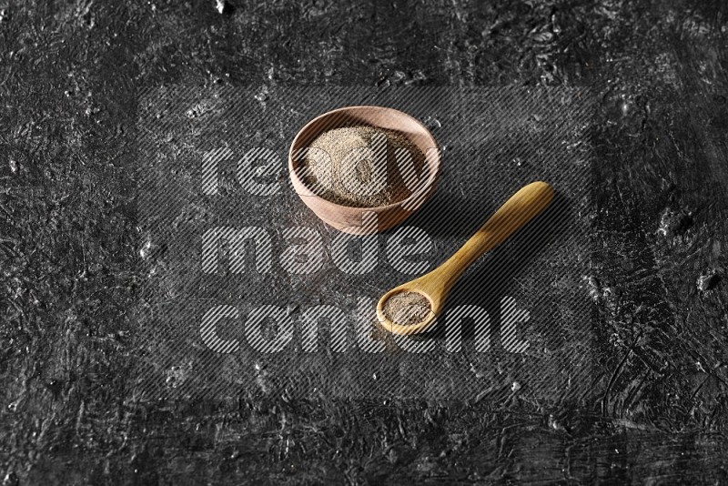 بودرة الفلفل الأسود في وعاء خشبي وملعقة خشبية علي خلفية سوداء