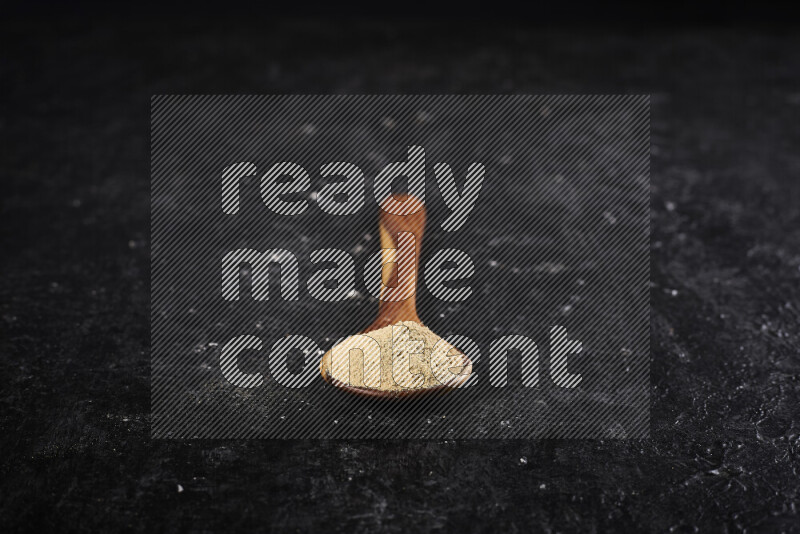 A wooden ladle full of ground ginger powder on black background