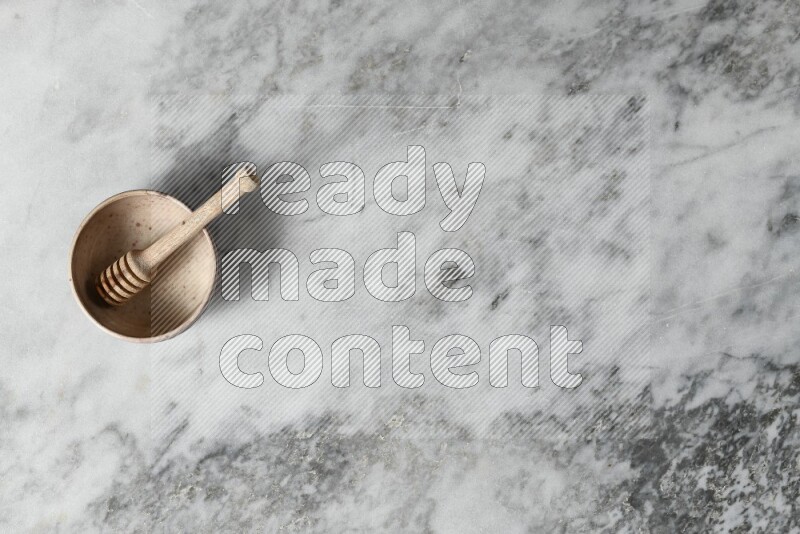 Beige pottery bowl with wooden honey dipper in it on grey marble background