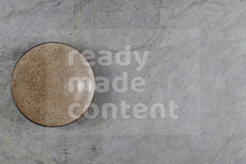 A beige pottery plate on grey marble background