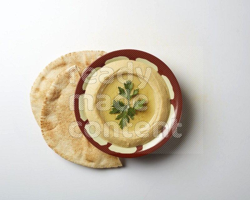 Hummus in a traditional plate garnished with parsley on a white background