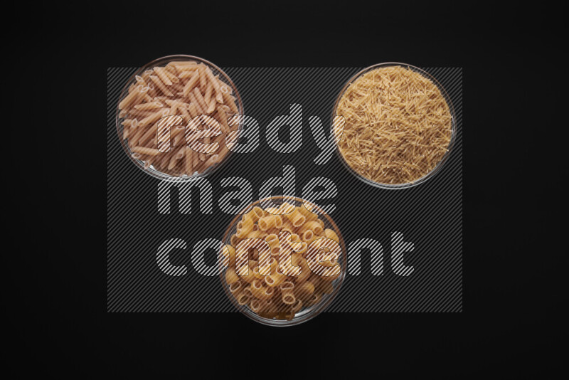 Different pasta types in glass bowls on black background