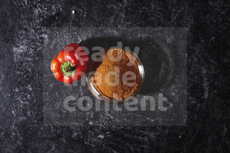 A glass bowl full of ground paprika powder on black background