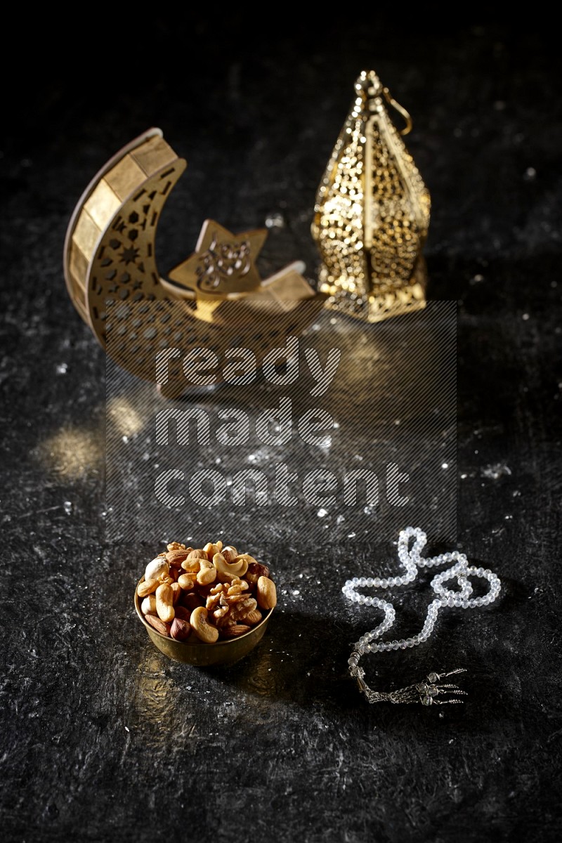 Nuts in a metal bowl with prayer beads beside golden lanterns in a dark setup