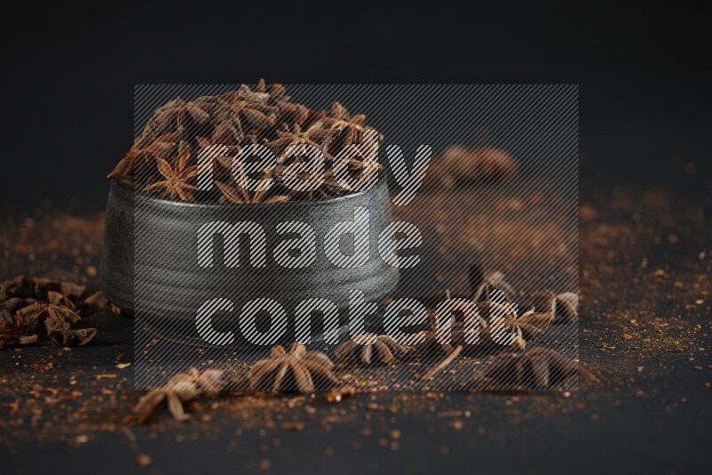 Star Anise in a black bowl with sprinkled anise on black flooring