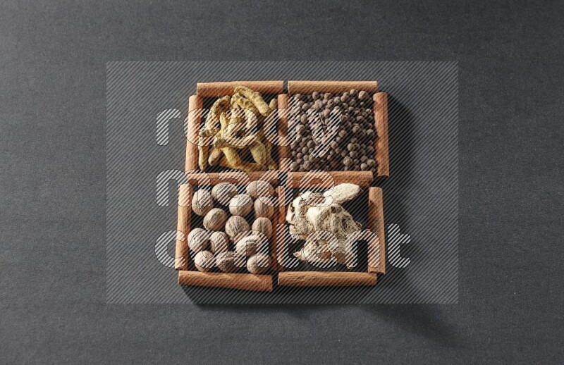 4 squares of cinnamon sticks full of turmeric fingers, allspice, dried ginger and nutmegs on black flooring