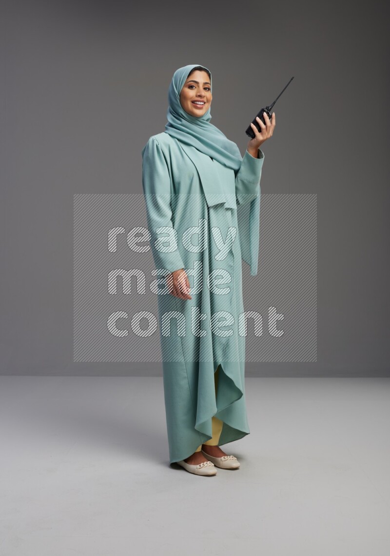 Saudi Woman wearing Abaya standing holding walkie-talkie on Gray background