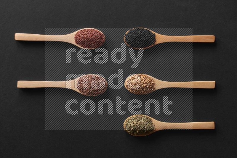 الفلفل الأسود وحبوب الخردل وحبة البركة وحب الرشاد والكمون و حبوب الكتان في معالق خشبية علي خلفية سوداء