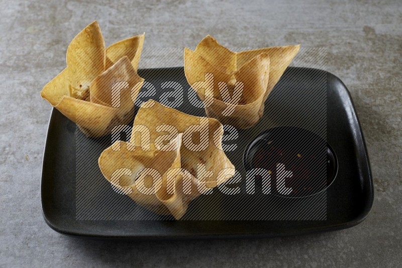 wonton cups with soy sauce ramkin on rectangle dark grey ceramic plate on grey textured counter top