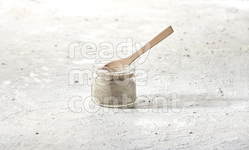 وعاء زجاجي وملعقة خشبية ممتلئان ببودرة الفلفل الأبيض على أرضية بيضاء