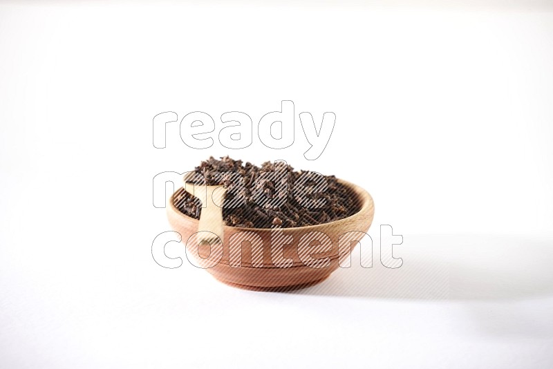 A wooden bowl and a wooden spoon full of cloves on a white flooring