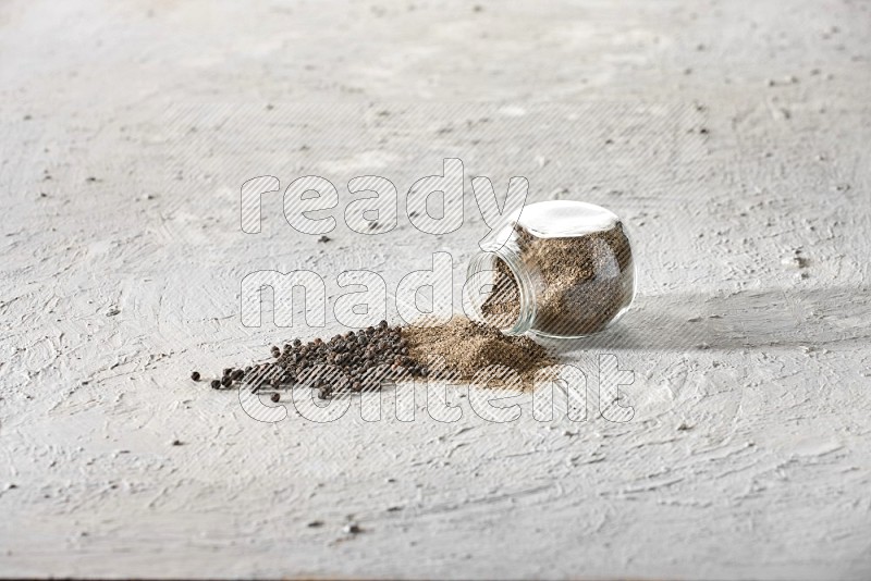 Flipped glass spice jar full of black pepper powder and paper beads beside it on a textured white flooring