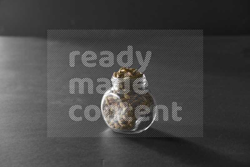 A glass spice jar full of cardamom on black flooring