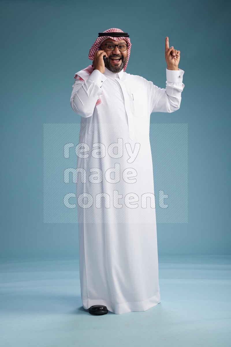 Saudi Man with shimag Standing talking on phone on blue background