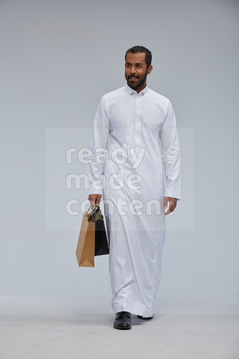 Saudi man Wearing thob standing holding shopping bag on Gray background