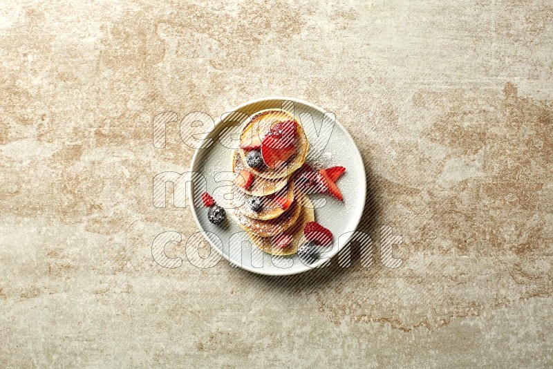 Five stacked mixed berries mini pancakes in a blue plate on beige background