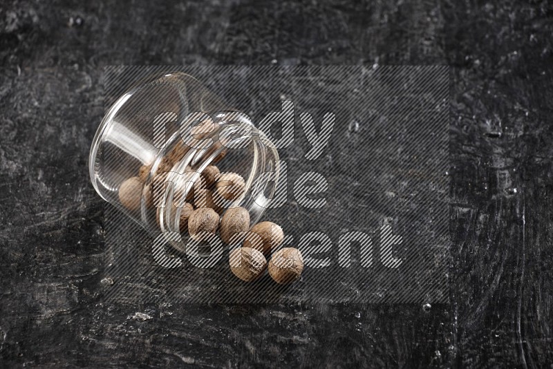 A glass jar full of nutmeg flipped and the seeds came out on a textured black flooring in different angles