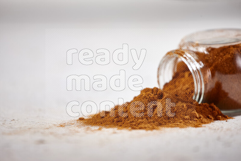 A glass jar full of ground paprika powder flipped with some spilling powder on white background