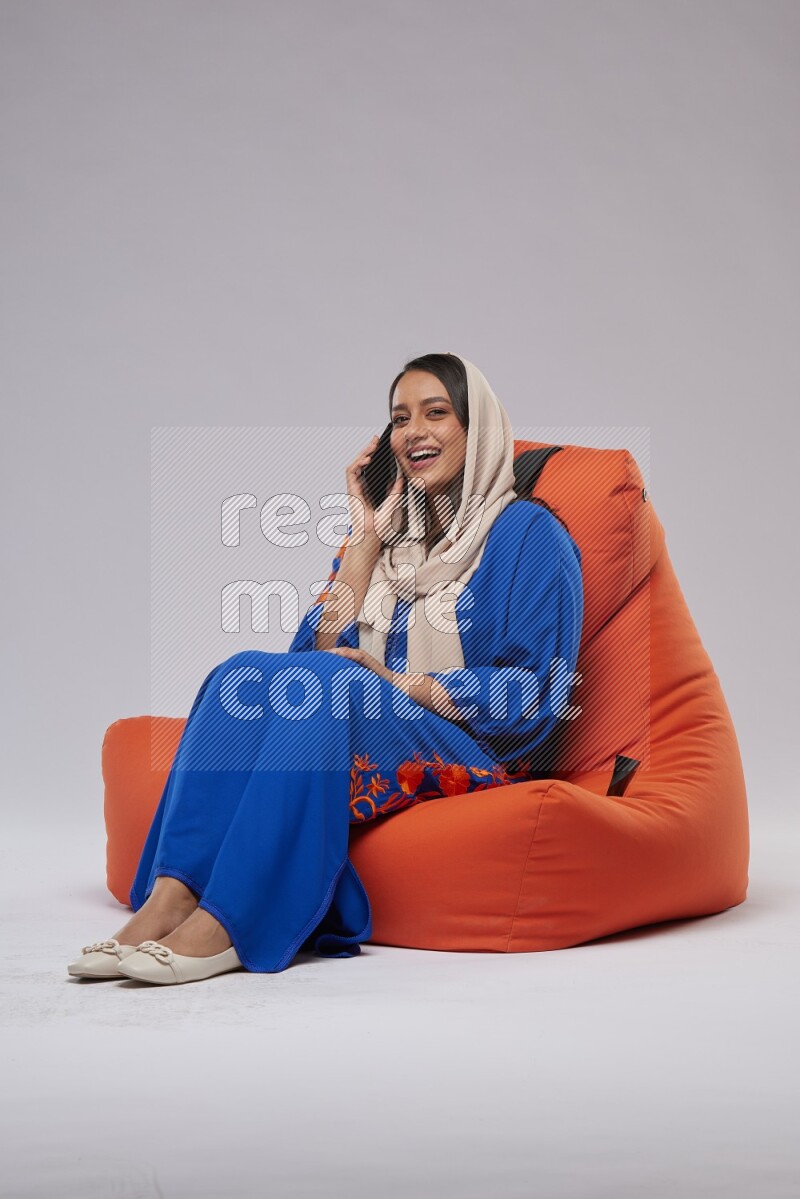 A Saudi woman wearing Jalabiya sitting on an orange beanbag and talking on the phone