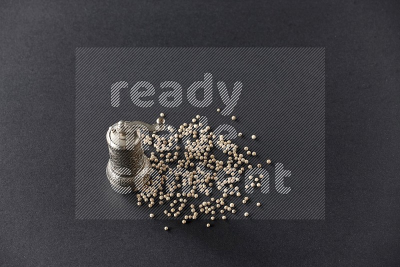 White pepper with a metal pepper grinder on black flooring