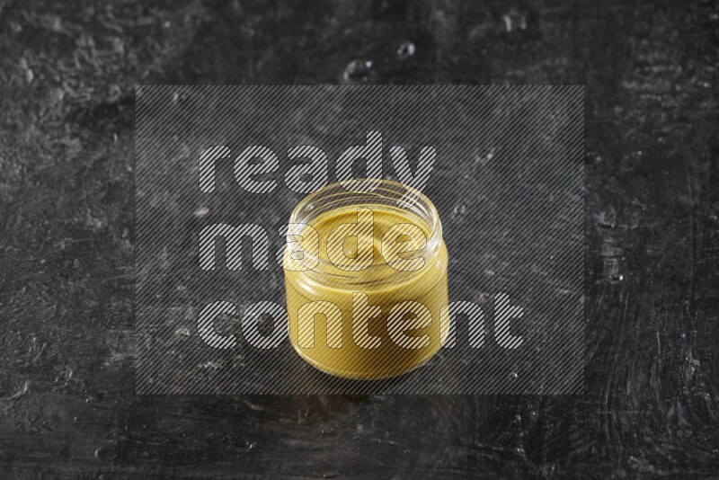 وعاء زجاجي ممتلئ بمعجون الخردل على خلفية سوداء