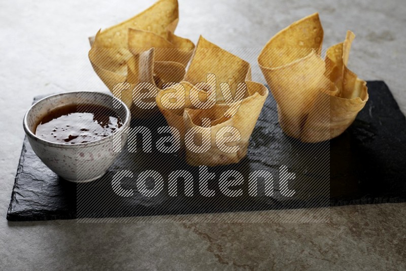 wonton cups with soy sauce ramkin on rectangle slate on grey textured counter top