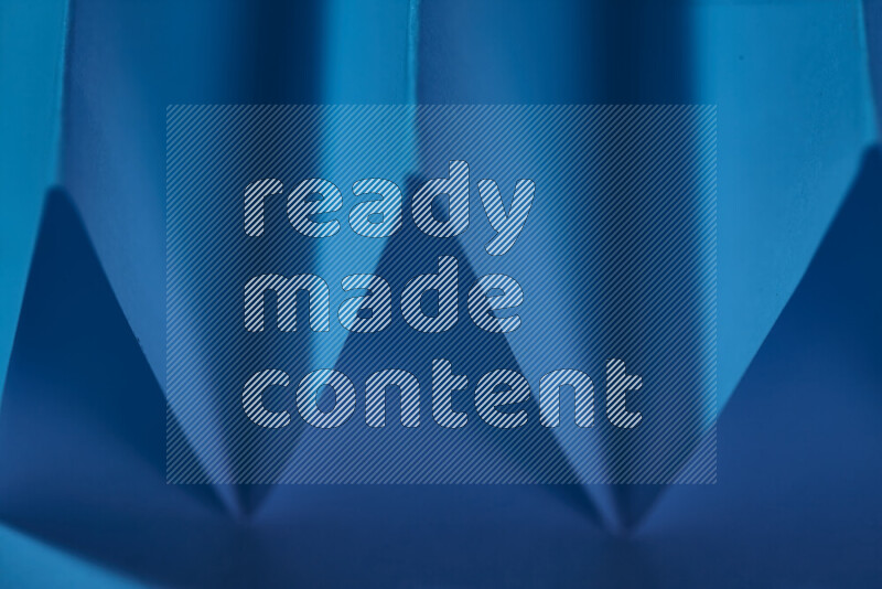 صورة مجردة مقربة تظهر طيات ورقية هندسية حادة بتدرجات اللون الأزرق