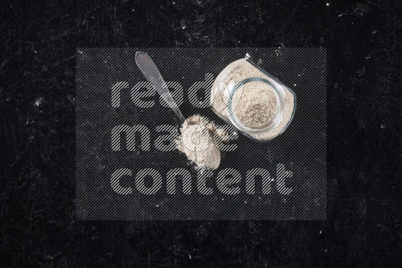 A glass jar full of onion powder on black background