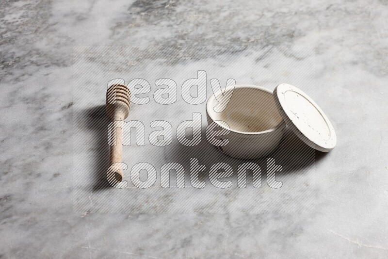 White pottery bowl with wooden honey dipper on the side on grey marble background