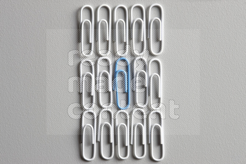 A bunch of white paper clips with a different colored paper clip in the center on grey background
