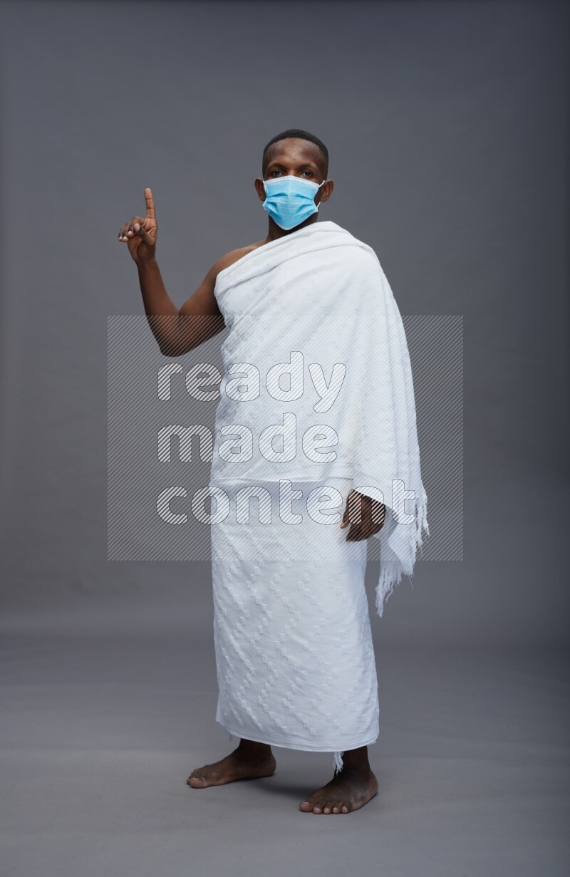 A man wearing Ehram with face mask Standing Interacting with the camera on gray background
