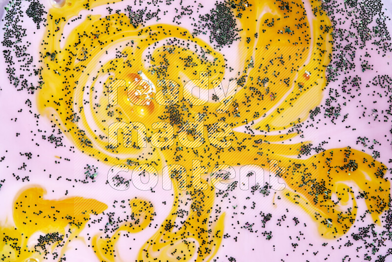 A close-up of sparkling green glitter scattered on swirling yellow and pink background