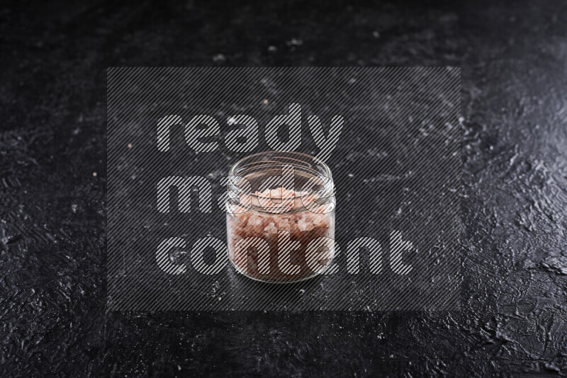 A glass jar full of coarse himalayan salt crystals on black background