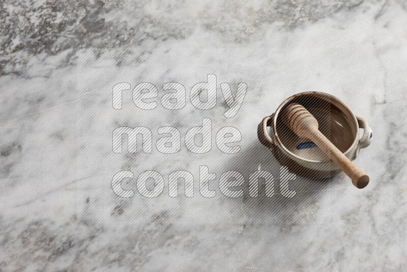 Multicolored pottery bowl with wooden honey dipper in it on grey marble background