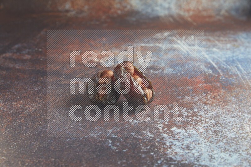 two hazelnut stuffed madjoul dates on a rustic reddish background