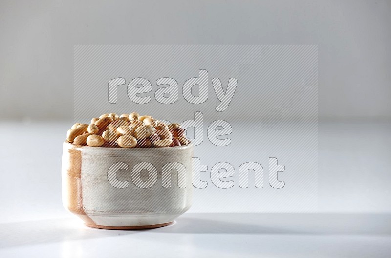 A beige ceramic bowl full of peeled peanuts on a white background in different angles