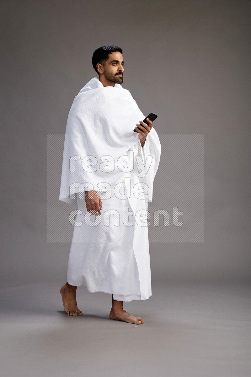 A man wearing Ehram Standing texting on phone on gray background