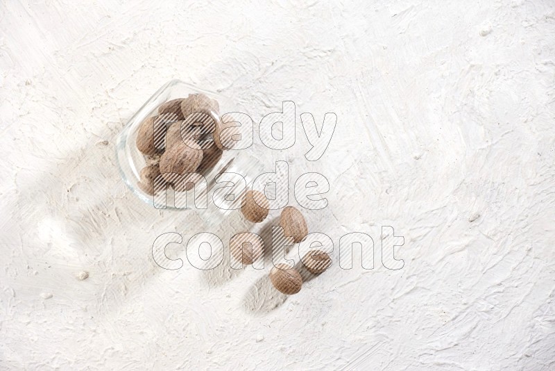 A glass spice jar full of nutmeg flipped and the seeds came out on a textured white flooring in different angles