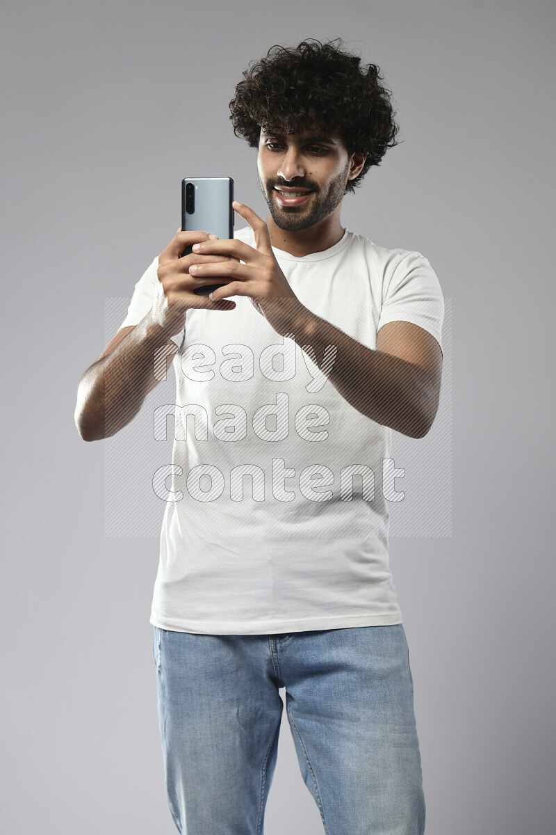 رجل يرتدي ملابس كاجوال يصور بهاتفه علي خلفية بيضاء