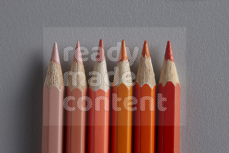 مجموعة من أقلام الرصاص الملونة مرتبة لتعرض تدرجا من الألوان البرتقالية علي خلفية رمادية